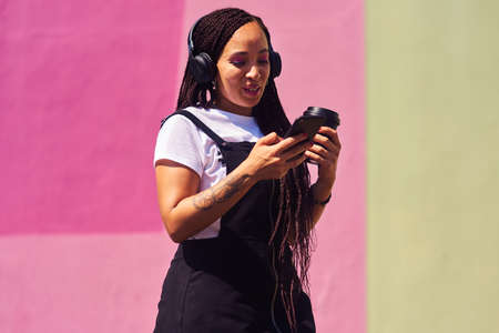 I am always social networking. an attractive young woman standing against a pink wall and using...