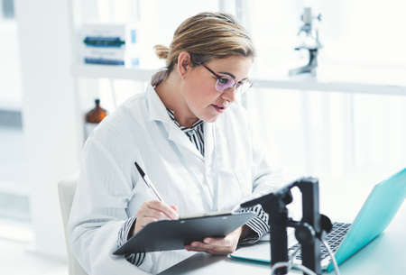 This looks like something Ive seen before. an attractive young female scientist filling a document while using a laptop in a laboratory.の写真素材