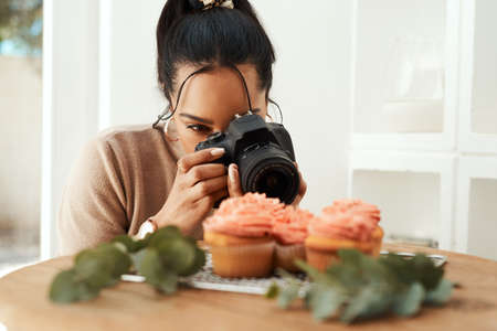 This is going to look so good on my blog. an attractive young businesswoman using her camera to photograph cupcakes for her blog.の写真素材