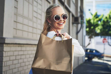 Follow me, Ive got a couple more shops to visit. Cropped portrait of an attractive young woman smiling while holding shopping bags in the city during the day.の写真素材