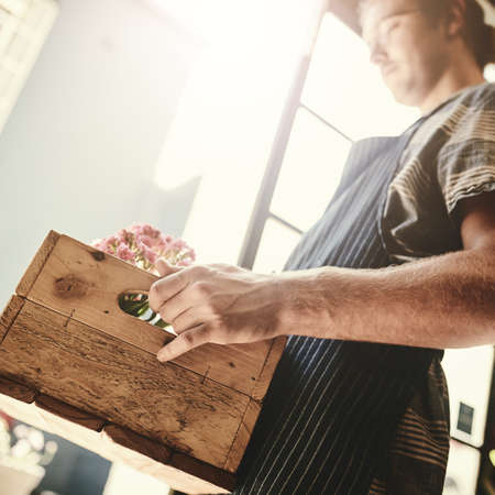 Stocked up and ready to bloom. a florist holding a crate full of flowers inside his plant nursery.