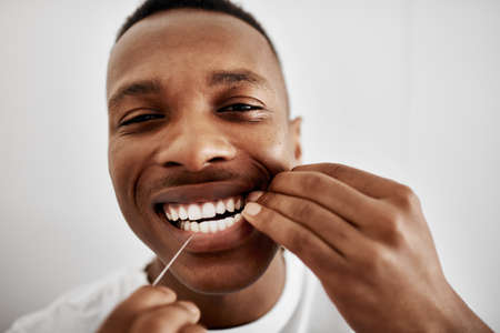 Floss for cleaner, healthier teeth. a young man flossing his teeth in the bathroom at home.の写真素材