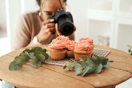 Making sure I get the right angle. an attractive young businesswoman using her camera to photograph cupcakes for her blog.の写真素材