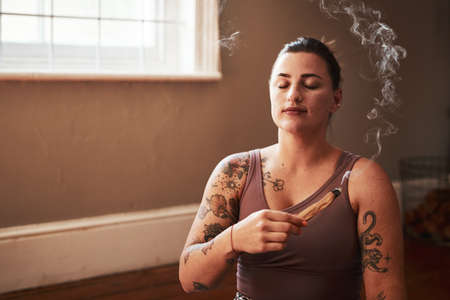 Meditation carries me more calmly through my day. a young woman burning a palo santo stick at home.の写真素材