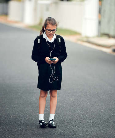 Just bumping my favorite jams on my way to school. Full length shot of a young schoolgirl listening to music and using her cellphone while walking to school.の写真素材