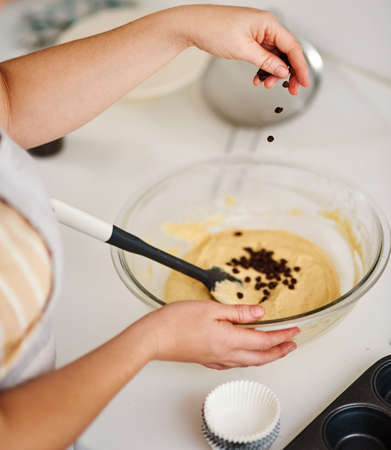 Adding some edible magic. a woman adding chocolate chips to her batter.の写真素材