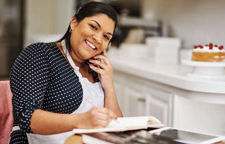 At this rate Ill have to hire some help. a making notes while talking on her cellphone.の写真素材