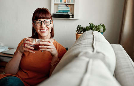 Smile, beautiful. a young woman enjoying a cup of tea while relaxing at home.の写真素材