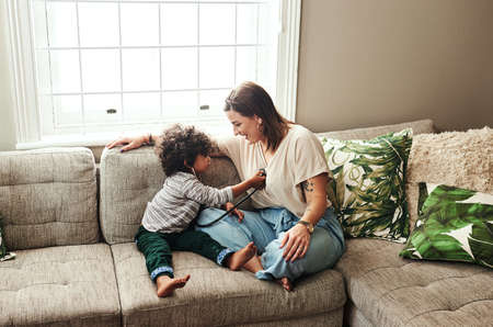 We have a little doctor in the making. a cheerful young woman and her son playing around with a stethoscope while being seated on a sofa at home during the day.の写真素材