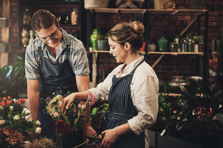 Our small business is flourishing. two young florists trimming flowers and working together inside their plant nursery.の写真素材