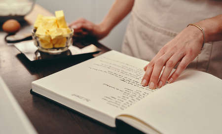 This recipe makes it all so easy. an unrecognizable woman reading a recipe from a book while baking...