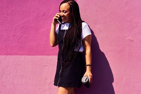 Staying in touch is so easy with technology. an attractive young woman standing against a pink wall...