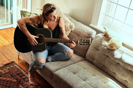 Some of the greatest hits were made at home. a young woman playing a guitar on a relaxing day at home.の写真素材