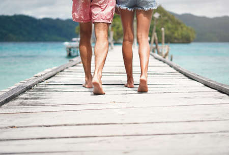 I will go anywhere with him. Rearview shot of an unrecognizable couple walking down a boardwalk overlooking the ocean during a vacation.の写真素材