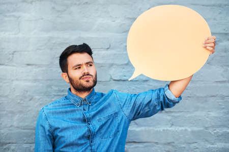 I dont quite believe that... a handsome young man looking skeptical while holding a speech bubble against a brick wall.の写真素材