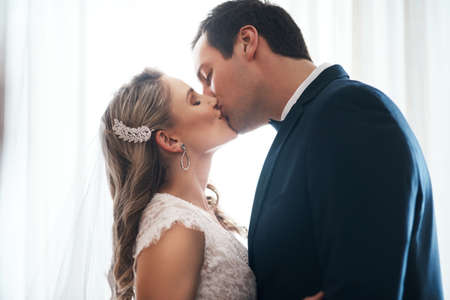 Sealed with a kiss. an affectionate young couple standing indoors together and kissing after their wedding.の写真素材