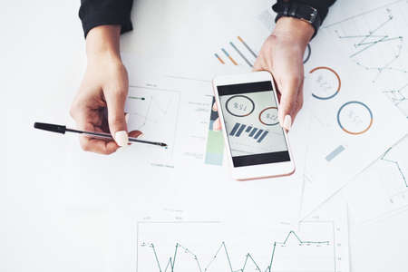 How are the stats looking so far. Closeup shot of an unrecognisable businesswoman using a cellphone while going through paperwork in an office.の写真素材