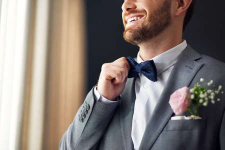 Hes all set to go and tie the knot. an unrecognizable bridegroom adjusting his bowtie inside a changing room on his wedding day.の写真素材
