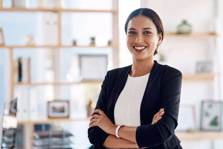 Success is a guarantee. Cropped portrait of an attractive young businesswoman standing with her arms folded in the office.の写真素材