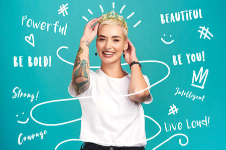 Flaunt your inner queen. Studio shot of a young woman putting a crown her head against a turquoise background.の写真素材