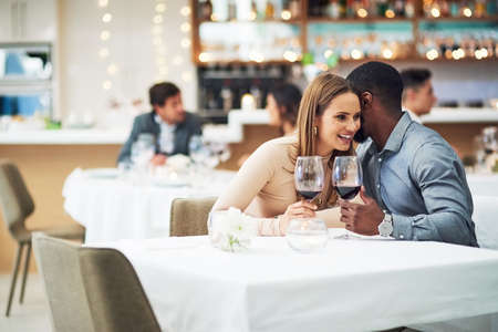 Hes ever so naughty. an affectionate young man whispering into his girlfriends ear while sitting in a restaurant.の写真素材