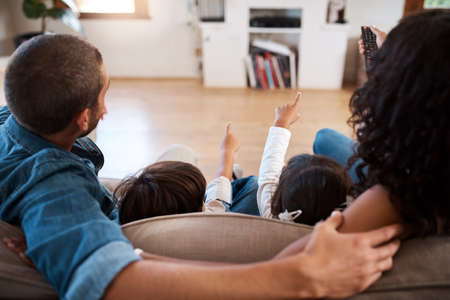 The kids always get to chose what to watch. Rearview shot of a couple watching something on the television with their two young kids.の写真素材