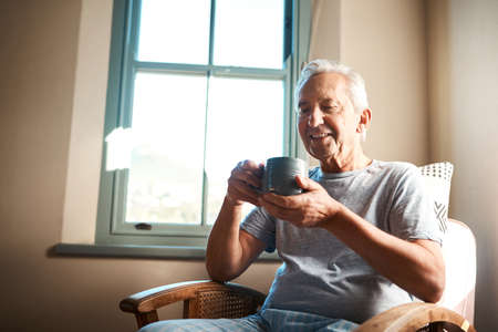 Hmm, nothing like a cup of coffee in the morning. a happy senior man holding a cup of coffee and sitting in an armchair at home.の写真素材
