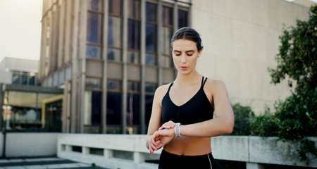 Keeping her fitness levels right on track. a young woman looking at her watch while exercising in the city.の写真素材