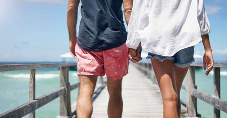 Love is being with you anywhere. Rearview shot of an unrecognizable couple walking down a boardwalk and holding hands during a vacation.の写真素材