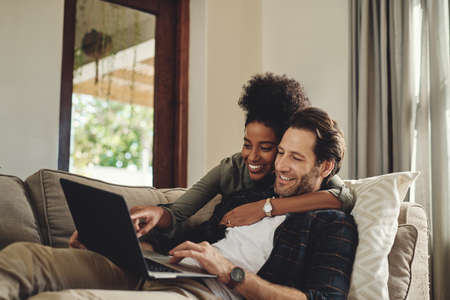 Have a look at that hunny. a happy young couple using a laptop while relaxing on a couch in their living room at home.の写真素材