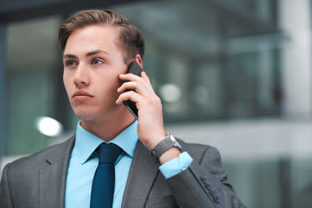 Hes got his business face on. a handsome young businessman standing alone in his office and using his cellphone.の写真素材