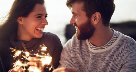 The sparkle in your eyes tells me that you love me. a young couple holding sparklers on the beach.の写真素材