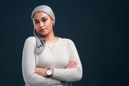I am proud to be muslim. an attractive young woman wearing a headscarf and standing with her arms folded against a black background.の写真素材