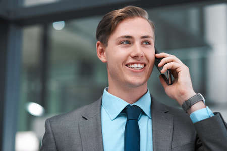 Thank you for your time. a handsome young businessman standing alone in his office and using his cellphone.の写真素材