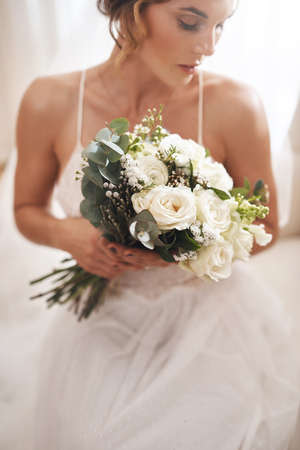 I cant wait to be his wife. an attractive young bride sitting alone in the dressing room and holding her bouquet of flowers.の写真素材