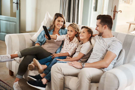 Weekend time is family time. a happy young family relaxing on the sofa and watching tv together at home.の写真素材