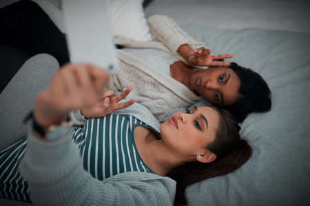 two young women lying taking selfies while lying on a bed.の写真素材
