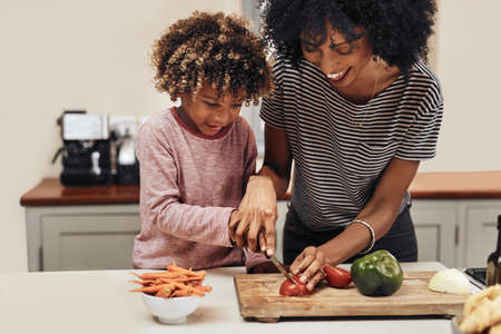 a young boy cutting vegetables with the assistance of his mother.の写真素材