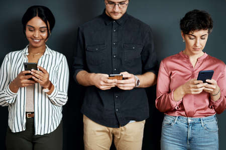 a diverse group of businesspeople standing against a gray background and texting on their cellphones.の写真素材