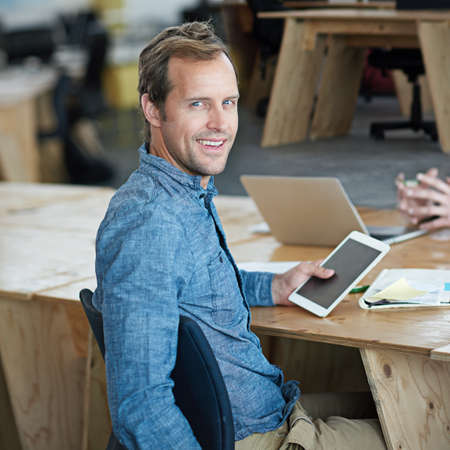 Confident marketing manager browsing the internet on a digital tablet in an office. Handsome and happy professional researching creative ideas to promote and advertise a startup on social mediaの写真素材
