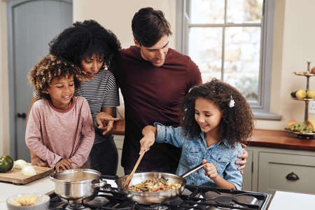 a family of four cooking together in their kitchen at home.の写真素材