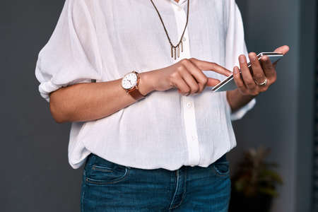 an unrecognizable businesswoman standing alone against a gray background and texting on her...