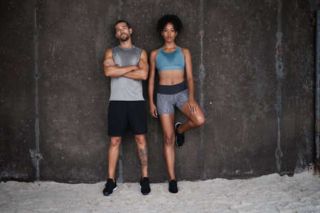 Whos up for a challenge against us. Full length shot of a sporty young couple posing against a wall while exercising inside a parking lot.の写真素材
