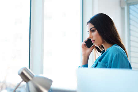 She wont let anyone step over her ambitions. a young businesswoman talking on a cellphone in an office.の写真素材