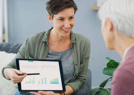 These projections look great. an attractive young woman showing a senior patient her medical results on a tablet while sitting down.の写真素材