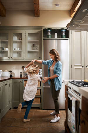I just want to see her light up with joy. a young girl and her mother dancing in the kitchen at home.の写真素材