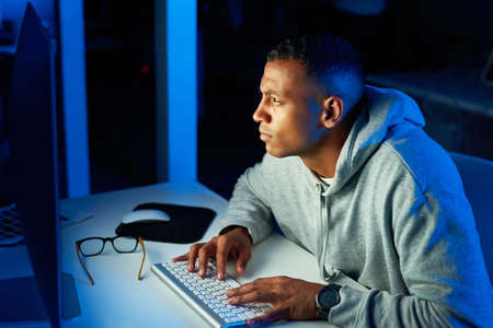 Hes got his eyes on his next victim. a young male hacker cracking a computer code in the dark.の写真素材