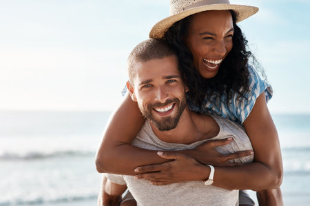 Love is such a blissful feeling. Portrait of a young man piggybacking his girlfriend at the beach.の写真素材
