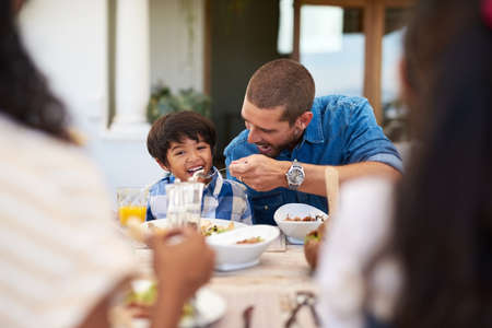 His appetite is growing bigger by the day. a father feeding his young son during a meal with family outdoors.の写真素材