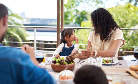 We always have the best of times together. an adorable little girl and her mother enjoying themselves during a meal with family outdoors.の写真素材
